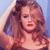 Pixelated image of a person with long brown hair wearing a light-colored top against a blue background.