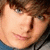 Pixelated close-up of a person's face with light skin, brown hair, and blue eyes, wearing a dark top against a blurred background.
