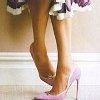 A close-up of a person's legs wearing a purple and white patterned skirt and pink high-heeled shoes, standing on a light-colored floor with a white baseboard.