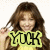 A pixelated image of a person with long brown hair wearing a yellow top, holding up a bright green sign with black text reading "YUCK".