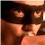 A pixelated close-up of a figure with dark hair and light skin, wearing a dark top with a light-colored collar, against a dark background.