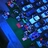 Pixelated abstract composition of blue, teal, and dark tones with scattered light blue, pink, and purple accents across a grid of square pixels.