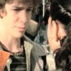 Two individuals in close proximity, one with light brown hair and the other with dark hair, both wearing hooded garments in muted tones.