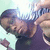 Pixelated image of a person with dark hair wearing a purple shirt, holding an object near their face against a light background.