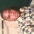 A pixelated image shows a person with light skin holding a small, round pink object against their chest while standing next to another figure in patterned clothing.