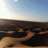 A pixel animated sequence showing a coastal scene with sand dunes, a rocky outcrop, and a white building under a blue sky, transitioning through lighting changes