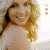 A pixelated image of a smiling woman with long blonde hair wearing a light-colored hat, viewed from the shoulders up against a bright background.