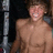 A pixelated static image shows a shirtless person with light skin and short brown hair standing against a dark background with a vertical metallic structure on the left.
