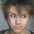 Pixelated close-up of a person with short brown hair and light skin, wearing dark clothing against a blurred background.