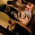 Pixelated static image of a character with light skin, brown hair, and dark clothing holding an object against a blurred background.