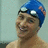 A person wearing a blue swim cap with white goggles and orange accents, smiling in three sequential poses showing head movement from left to right.