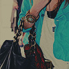 A person wearing a turquoise jacket over a white shirt with a small dark logo, holding a black bag with red and white patterns and a beaded chain accessory.