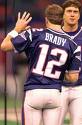 Static image of two football players in dark blue jerseys with white text and numbers, one player facing away showing "BRADY" and 12 on his jersey while the other faces forward with an open mouth gesture.