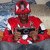 A person in a red helmet and jersey holds a game controller, seated against a blurred background with blue and beige tones.