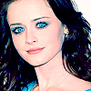 A static image of a person with long dark hair, blue eyes, and light skin, wearing a blue garment and a thin necklace.