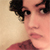 Pixelated close-up of a person's face with dark hair and light skin, wearing a red garment against a beige background.