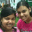 Two people in close proximity, one wearing a pink top, the other in green, with blurred background elements.
