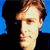 Pixelated close-up of a person's face with light brown hair, set against a blue background with dark areas on the sides.