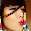 A close-up of a person with dark hair and red lips making a kissing face, wearing a colorful patterned garment.