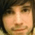 Pixelated close-up of a person's face with light skin tone, dark hair, and a neutral expression, set against a dark background.