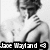 Black-and-white pixelated image of a person with short hair wearing a white shirt and dark tie, with text at the bottom reading "Joe Mayland" and a small arrow symbol.