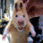 Animated cartoon character with light brown fur, large dark eyes, and a wide open mouth showing pink interior, arms raised in front of body.
