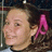 A static pixelated image shows a person with light skin and dark hair wearing a pink bow on the right side of their head, set against a blurred background.