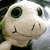 Animated plush toy with large green eyes and a stitched smile, showing subtle head movement across frames.