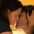 Two figures in close physical proximity with dark hair, one figure's mouth near the other's face against a gradient background transitioning from yellow to dark blue.