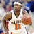 Pixelated image of a basketball player in white jersey with orange number 11, holding an orange basketball, wearing headband and red wristbands.