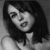 Black-and-white pixelated static image of a person with shoulder-length dark hair wearing a light-colored top, captured in grayscale tones with visible dithering and low-resolution rendering artifacts.