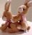 Pixelated static image of two brown rabbits in a close embrace with one rabbit's head resting on the other's shoulder, set against a light background.