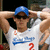 Pixelated image of a person wearing a blue cap and white jersey with blue and red text, arms raised behind head.