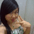 Pixelated image of a person with long dark hair in a silver dress, making a hand gesture near their face against a light background.