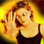 Pixelated image of a person with light brown hair wearing a dark tank top, holding a hand near their face against a yellow-orange gradient background.