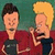 Static pixelated cartoon image of two characters with exaggerated facial features against a green background, one in red shirt and dark pants, the other in maroon top and black shorts.