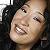 Pixelated close-up of a person's face with dark hair, showing teeth in a wide smile against a dark background.