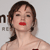 Pixelated image of a person with brown hair styled in a side braid, red lips, and a light-colored top against a plain background.