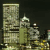 Pixelated cityscape with tall buildings, a domed structure, and a smaller tower against a dark background.