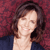 A pixelated portrait of a person with shoulder-length brown hair, wearing a dark blue top against a maroon background.