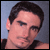 Pixelated static image of a person's head and shoulders with dark hair, visible ear, and partial shoulder in black clothing against a gradient background.