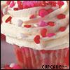 A close-up of a cupcake with white frosting, red heart-shaped sprinkles, and a red wrapper, with text reading "CUPCAKE!-" at the bottom.