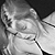 Pixelated grayscale image of a person with light hair, wearing a white garment and dark accessories, positioned against a gradient background.