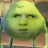 Pixelated green character with closed eyes and a neutral expression, wearing a pinkish garment against a blurred background.