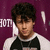 Pixelated image of a person with dark curly hair wearing a white shirt and black vest against a purple background with partial text.