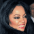 Pixelated close-up of a person with dark hair and red lips smiling, set against a dark background with a partial figure on the right.