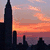 Pixelated cityscape at sunset with skyscrapers silhouetted against orange and purple sky, text overlays in white pixel font.