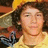 Pixelated image of a person with dark curly hair wearing a light-colored shirt, holding a dark object with a blue accent against a blurred background.