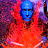 Pixelated static image of a blue-skinned figure with red-orange body against purple-pink background, likely representing the Blue Man Group mascot in low-resolution digital art style.