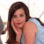 A pixelated image of a woman with long brown hair resting her chin on her hand, wearing a light blue sleeveless top against a bright background.